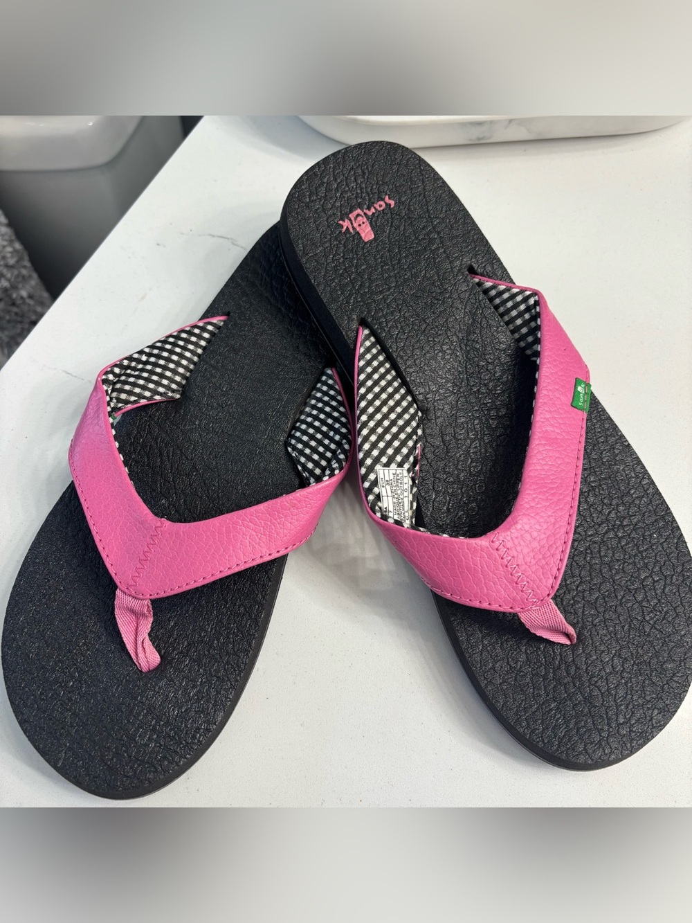 Classic black Sanuk flip flops. Striped fabric on the straps with pink strap.